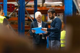 Frau und Mann schauen sich Daten auf einem Tablet in einer Lagerhalle an